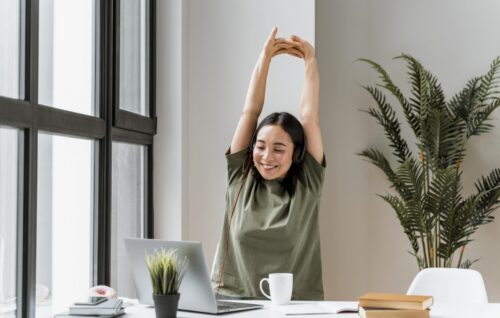 Ginástica laboral: mulher em frente ao computador alongando os braços